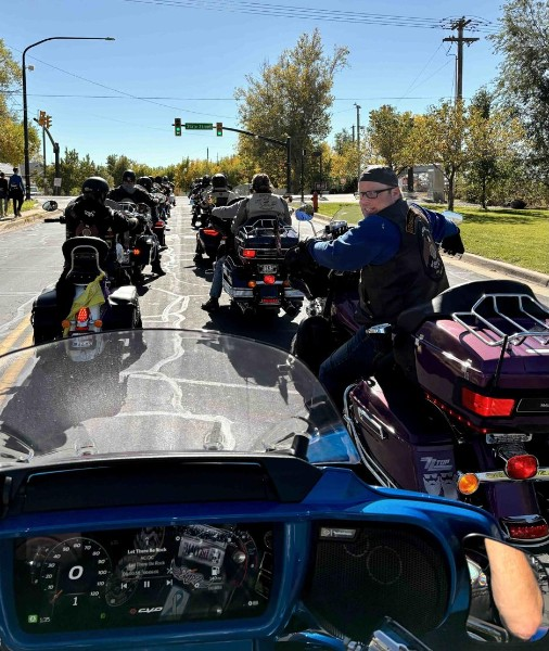 Motorcycle riders together on a sunny street, photographed from a blue motorcycle